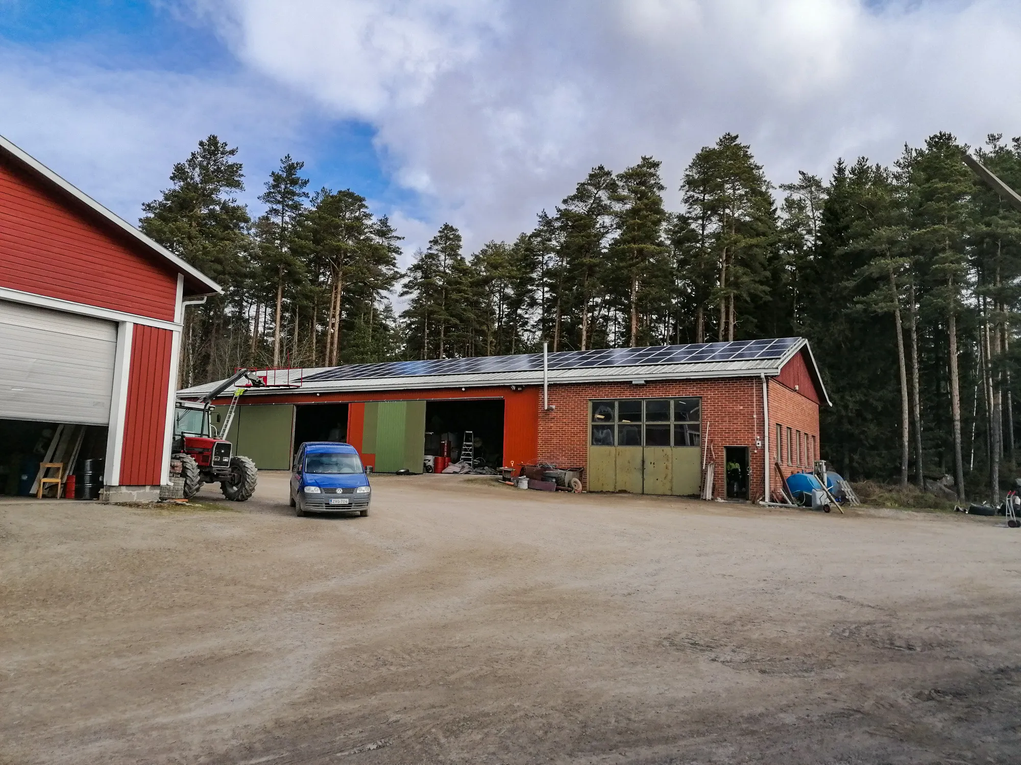 Tiilirakennuksen katolla on aurinkopaneeleja, ja sen edessä on traktori sekä pakettiauto.