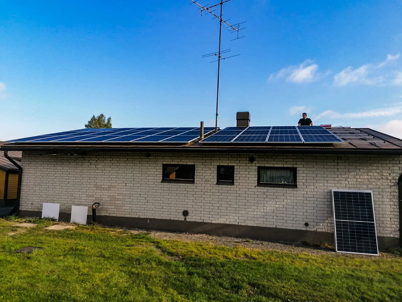 Mies asentaa aurinkopaneeleja talon katolle, jossa on käynnissä aurinkovoimalan asennus.