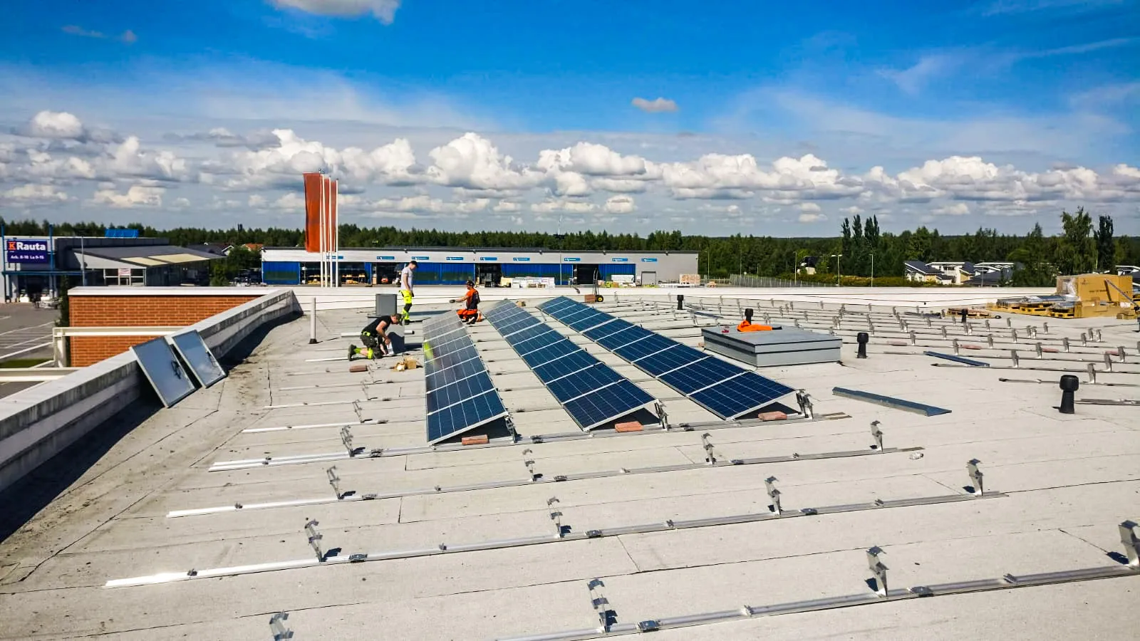Työntekijät asentavat aurinkopaneeleja suuren rakennuksen katolle osana aurinkovoimalan rakentamista.